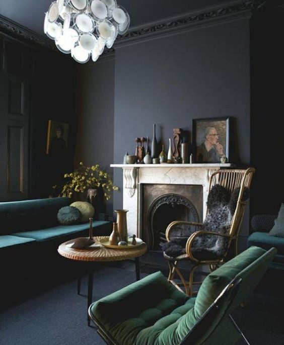 Dark-toned living room with deep green velvet furniture, a vintage marble fireplace, and a statement chandelier.