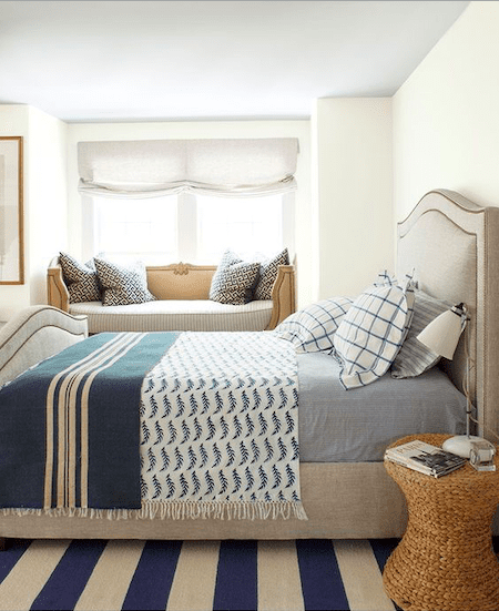 Cozy bedroom with neutral-toned upholstered bed, blue and white patterned bedding, and a built-in window seat with decorative pillows.
