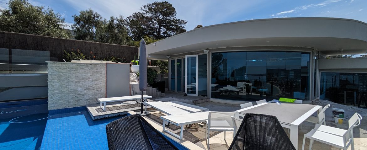 Modern poolside with a sleek design, contemporary outdoor furniture, and expansive glass windows.
