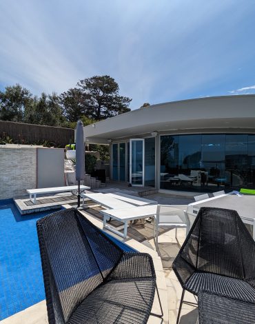 Modern poolside with a sleek design, contemporary outdoor furniture, and expansive glass windows.