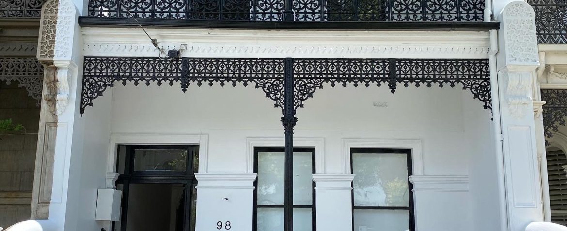 Victorian-style two-story house with black wrought iron balconies and a front garden.
