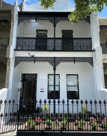 Victorian-style two-story house with black wrought iron balconies and a front garden.