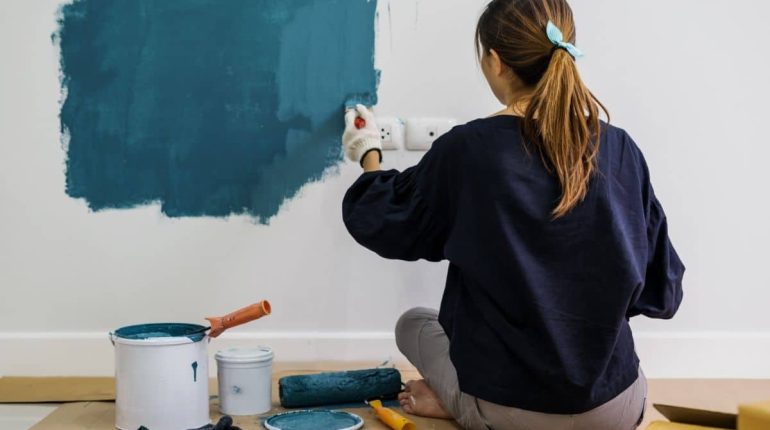 Woman Painting Wall With Blue Paint During Interior Renovation
