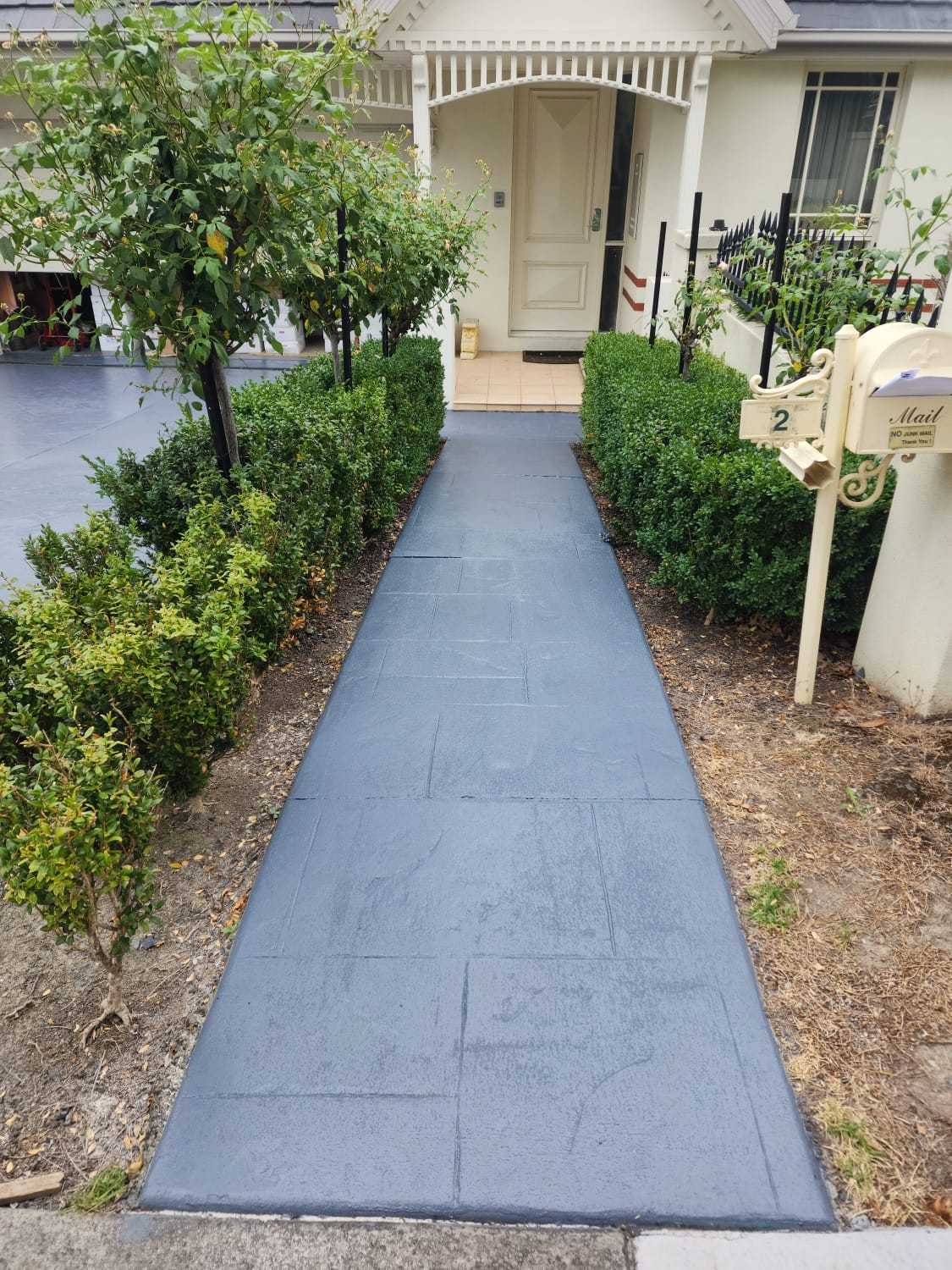 Freshly painted concrete walkway bordered by neat green hedges