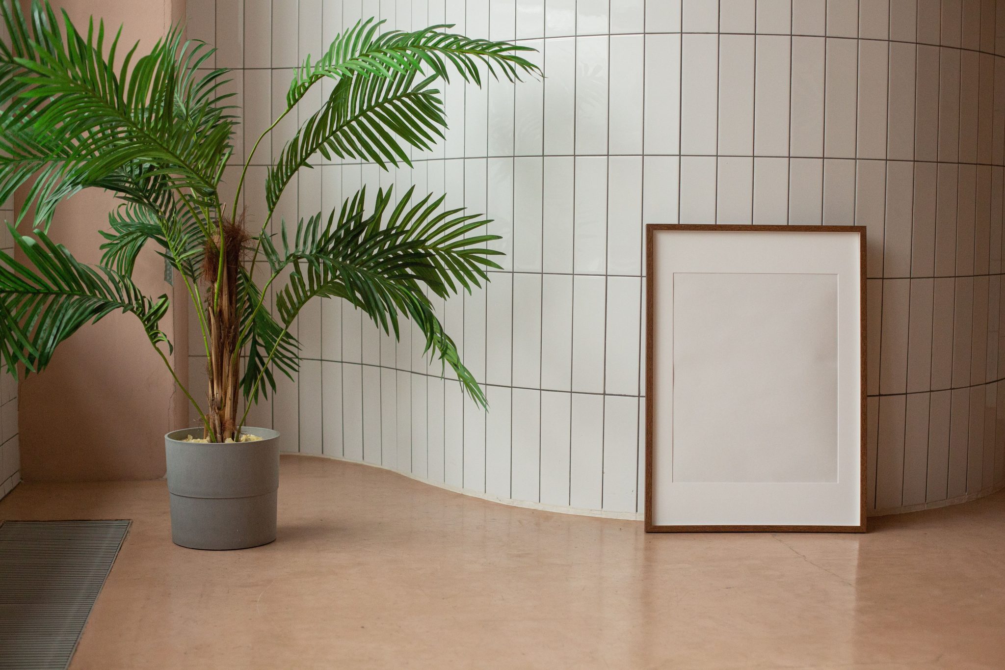 Modern interior with a potted plant and an empty framed picture leaning against a wall with sleek white tiles.