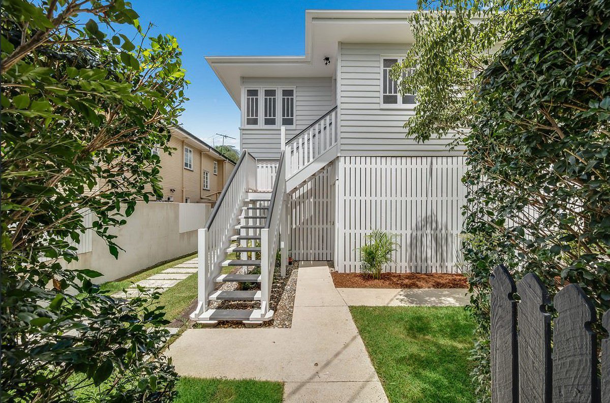 Freshly painted modern Queenslander-style home with a bright white exterior, elevated entrance, and lush greenery.