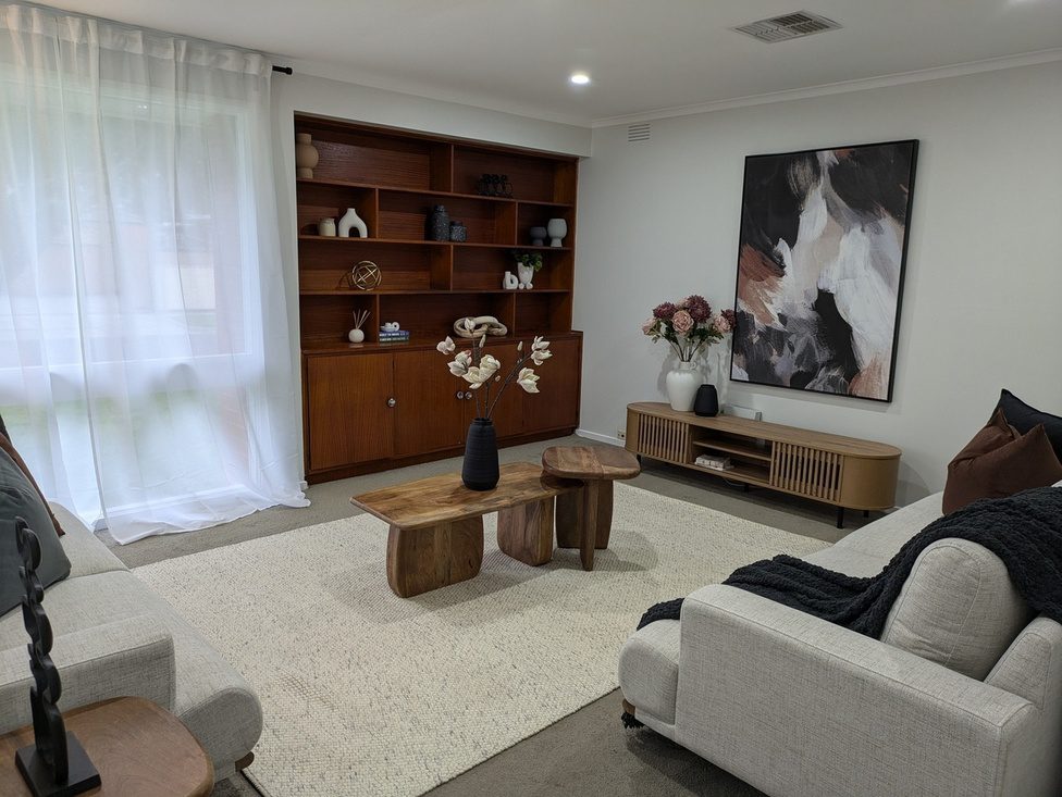 Stylish modern living room with neutral tones, wooden furniture, abstract artwork, and soft natural lighting.