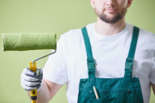 Painter Holding a Green Paint Roller Against a Freshly Painted Wall