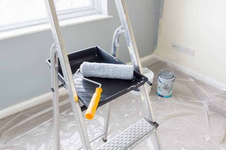 A paint roller and tray on a metal ladder during an interior wall painting project.