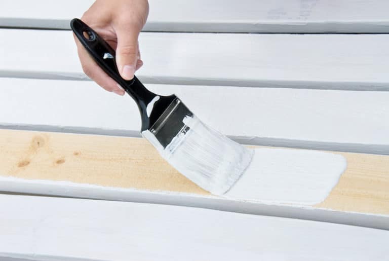 A person painting a wooden surface with white paint using a paintbrush.
