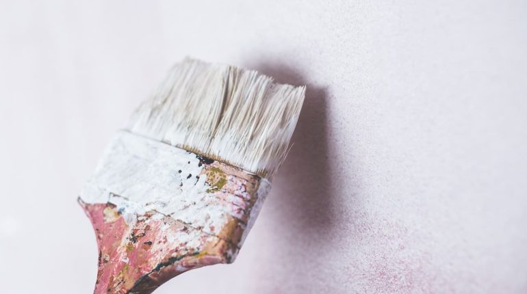 Close-up of a paintbrush applying light pink paint on a wall.