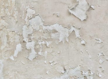 Peeling paint on a damaged wall showing cracks and flaking layers.