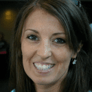 A smiling woman with long brown hair wearing silver earrings.