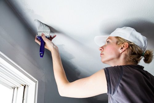 Woman Painting Ceiling With Brush in a Gray Room