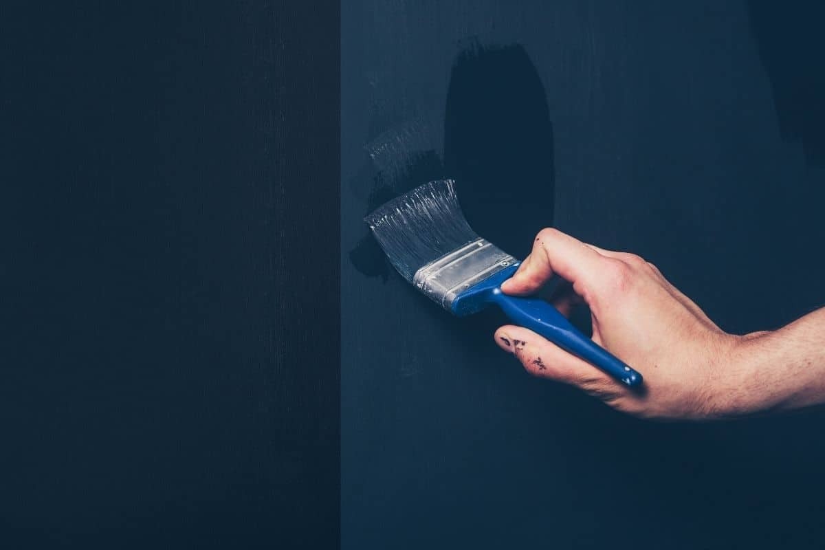 hand overbrushes blue paint onto a wall