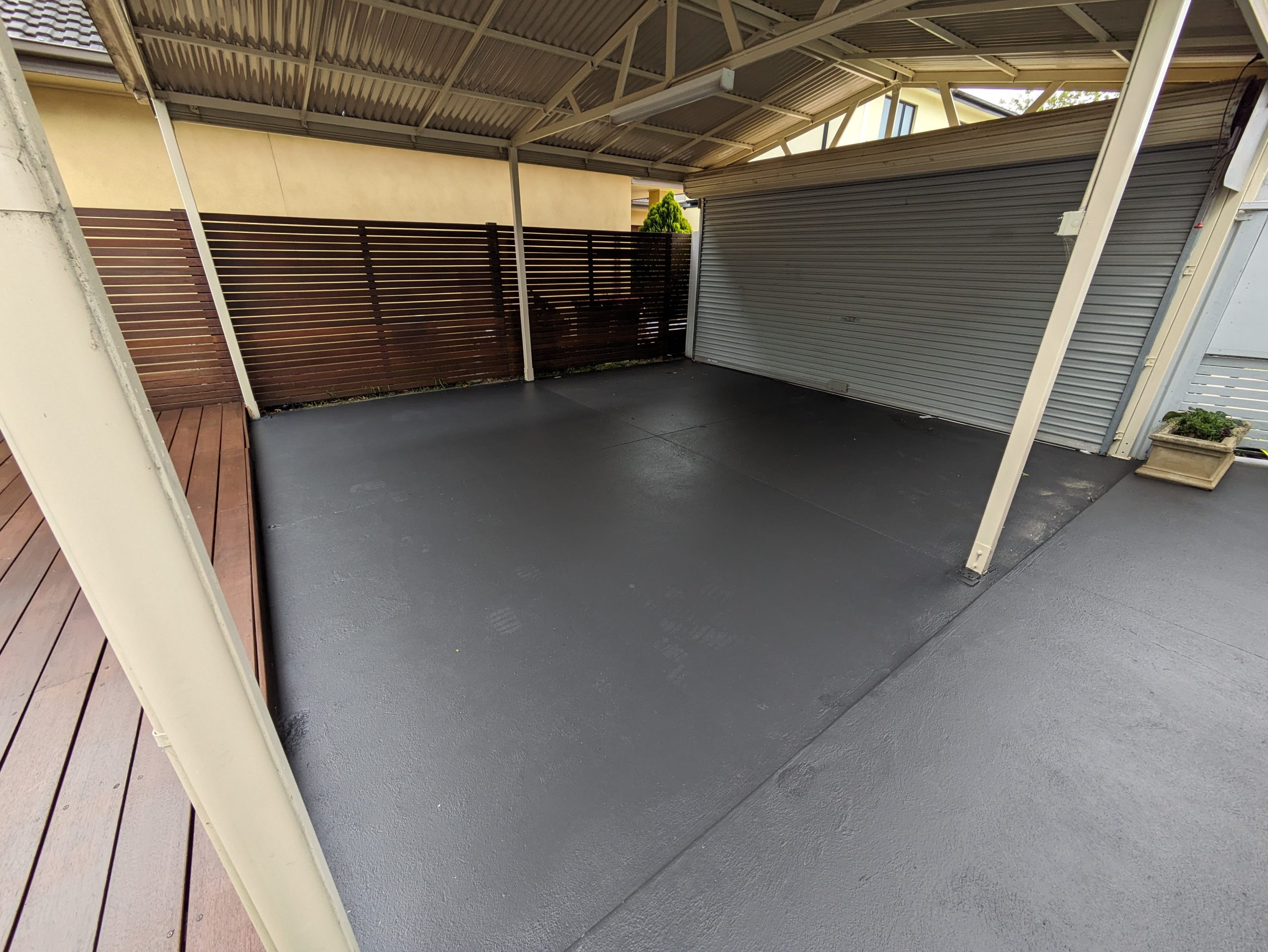 Professional garage floor painting in dark gray finish under covered carport area with modern fencing