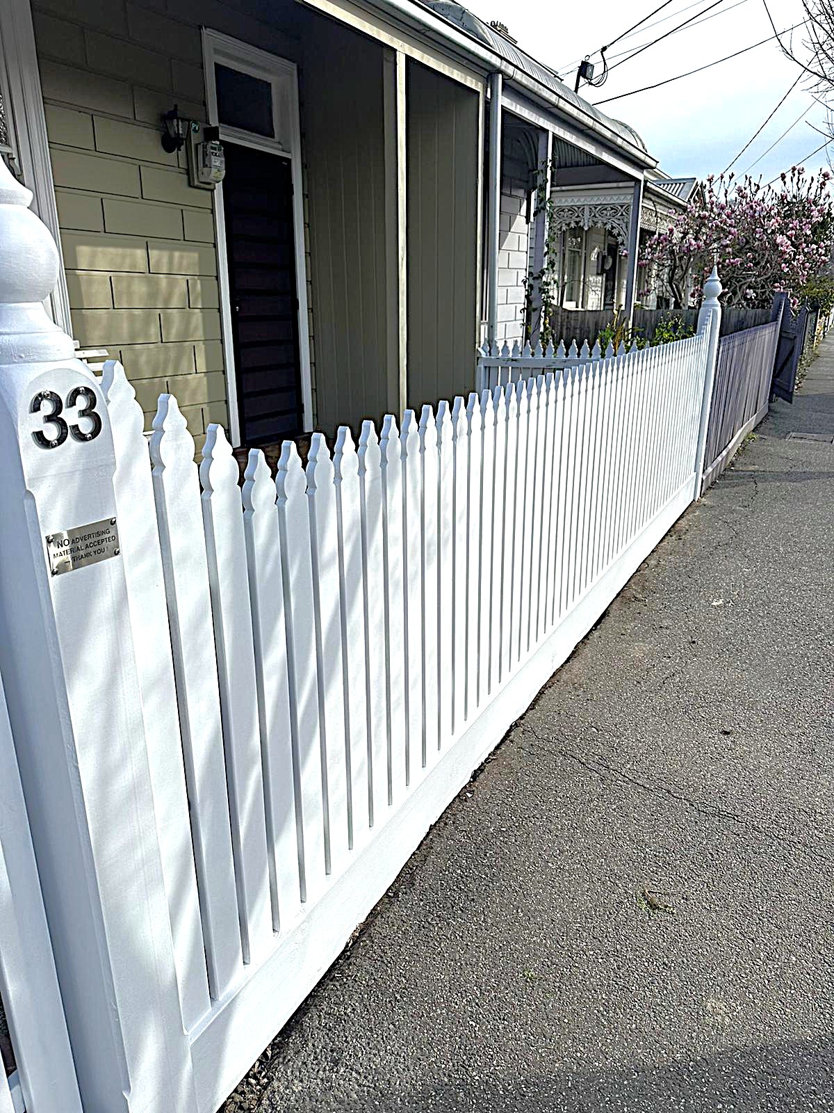 Alt Text: "Freshly painted white picket fence with decorative post caps along residential street