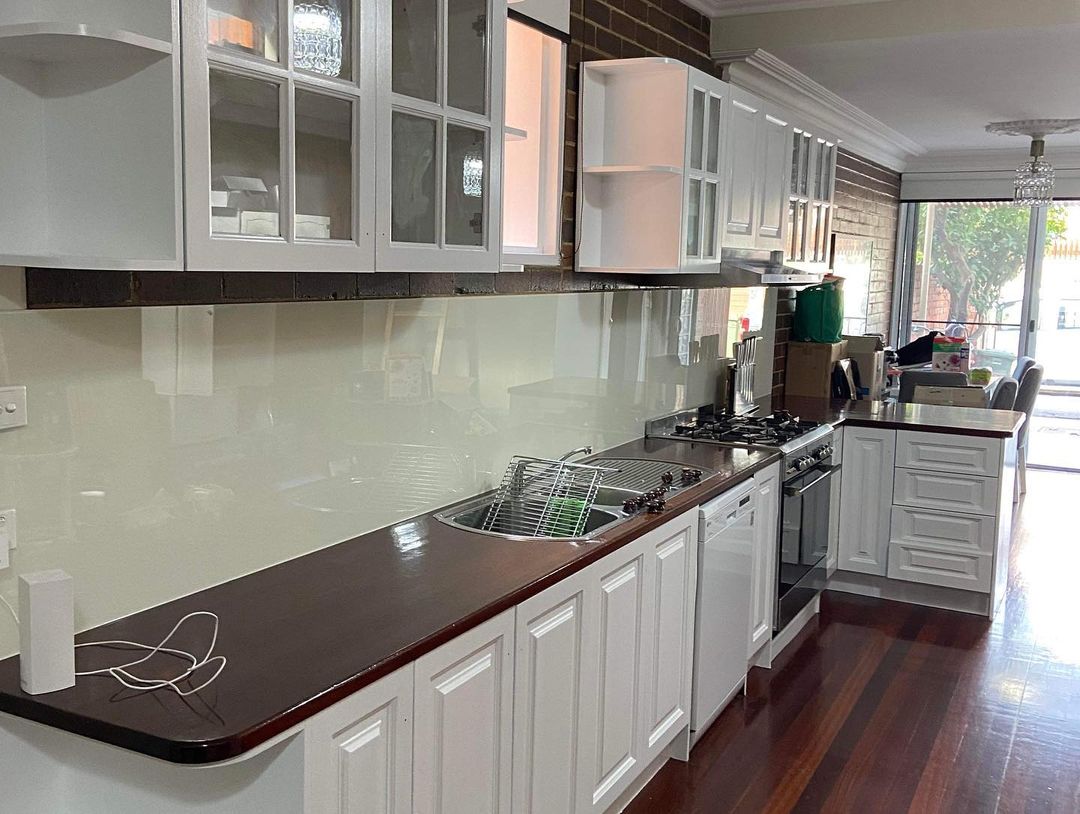 Freshly painted white kitchen cabinets with glass splashback and dark countertops showcasing professional interior painting