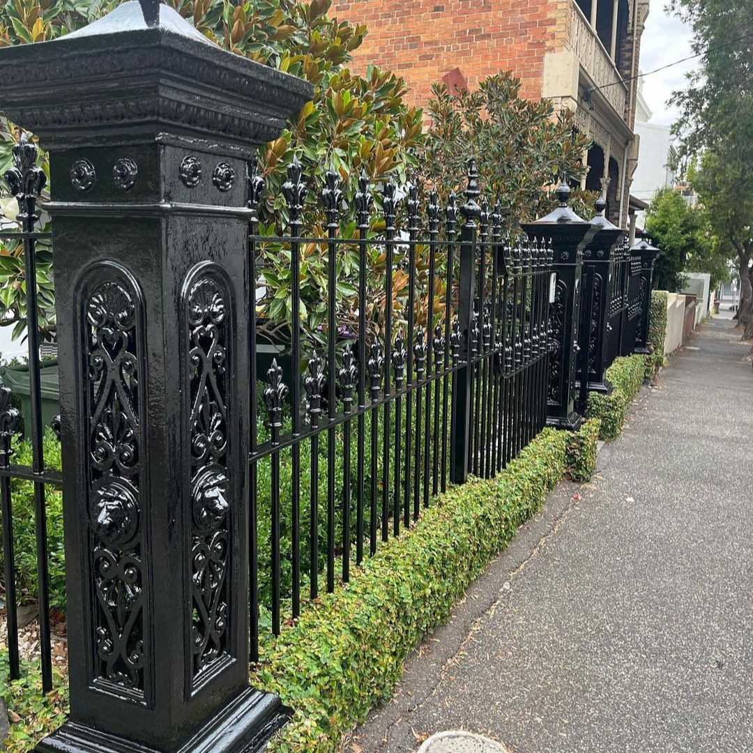 Black ornate cast iron fence with decorative scrollwork and fleur-de-lis details, professionally painted by Newline Painting, extending along residential sidewalk